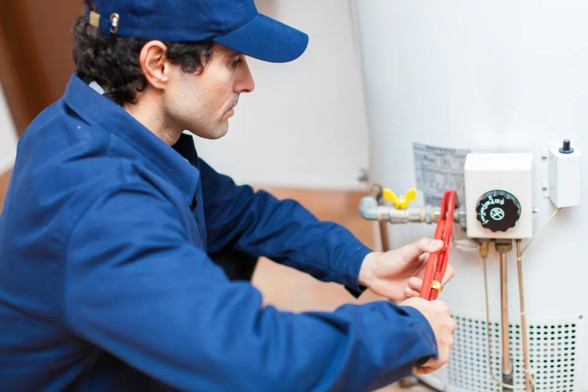 An ARS technician uses a wrench to adjust a valve to repair a water heater in a home.