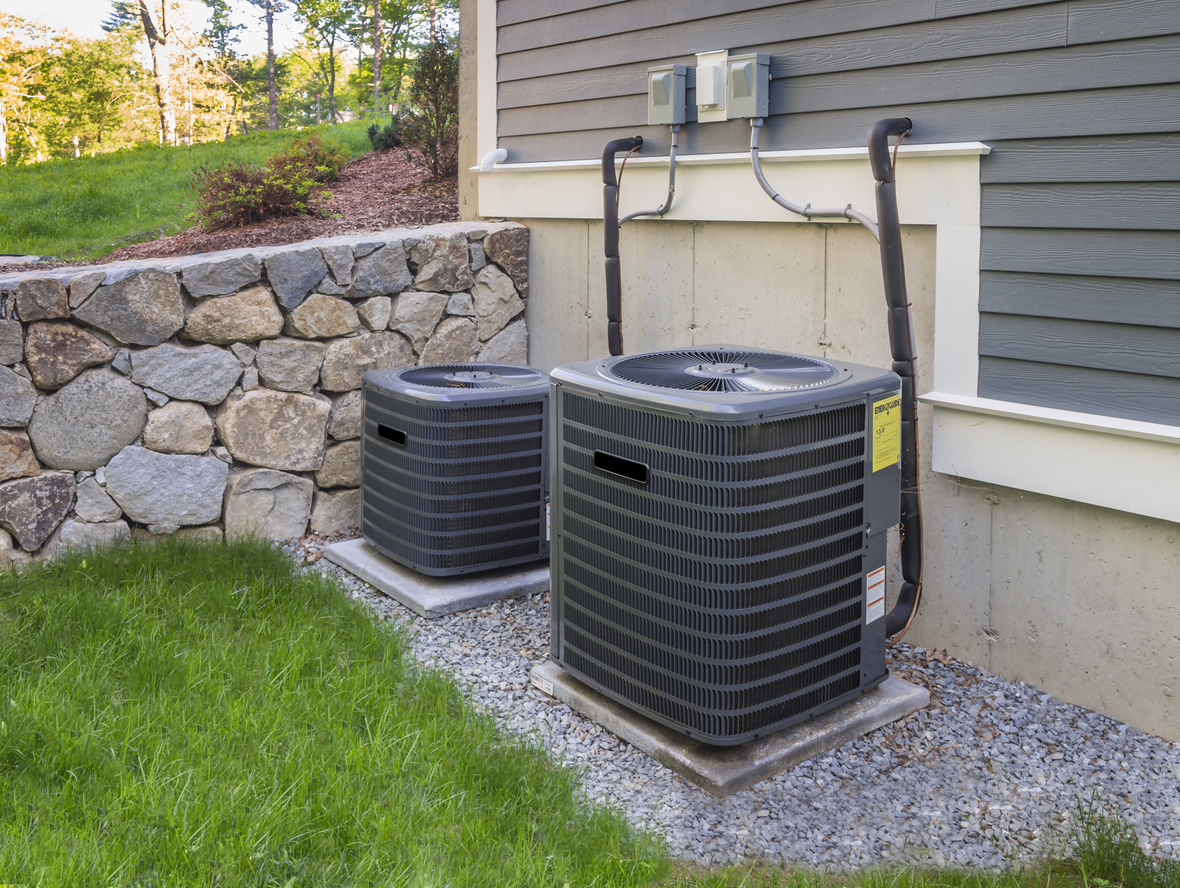 Two outdoor HVAC condenser units installed side by side on concrete pads next to a house.