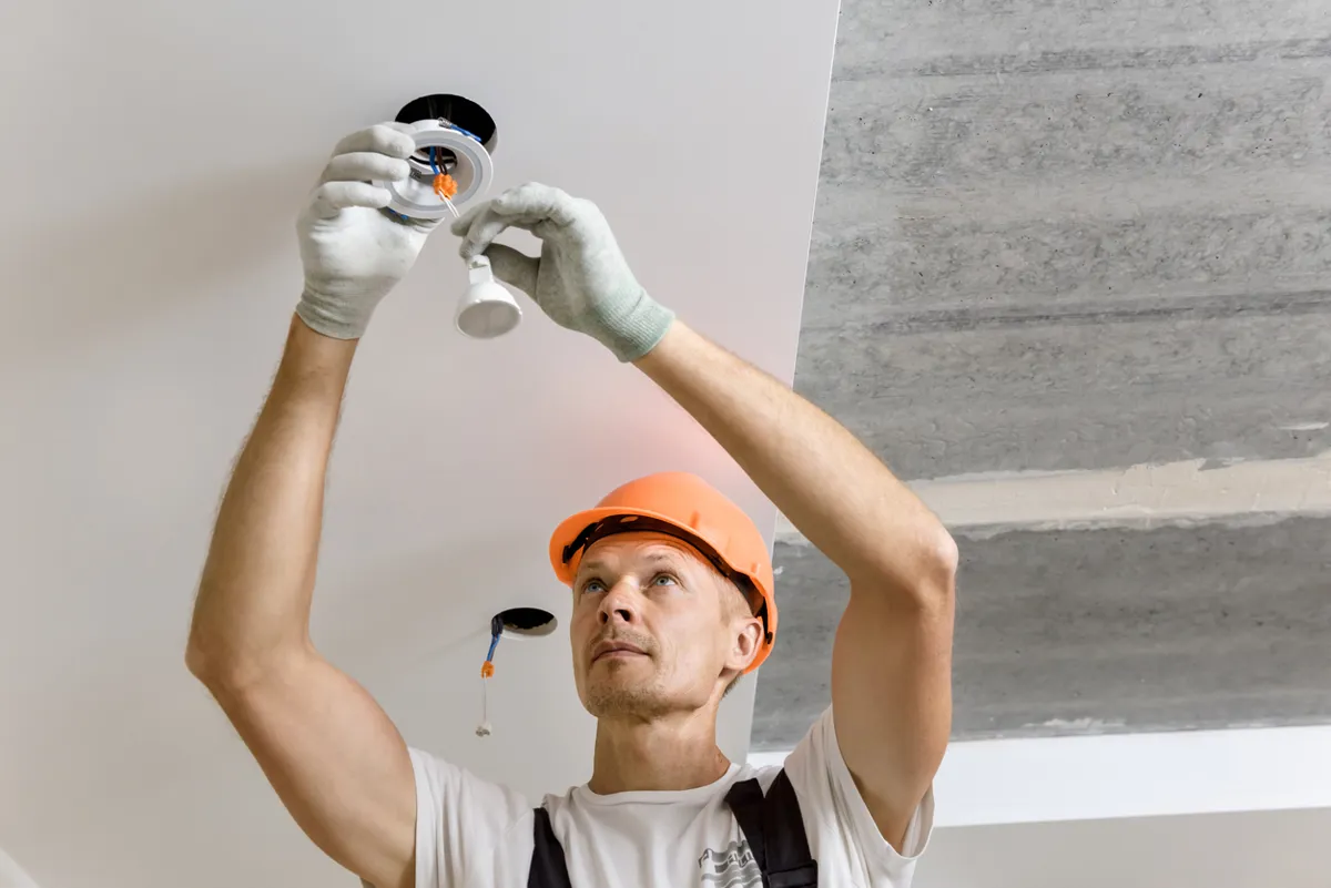 An ARS technician reaching to the ceiling, installing recessed lighting for a commercial company.