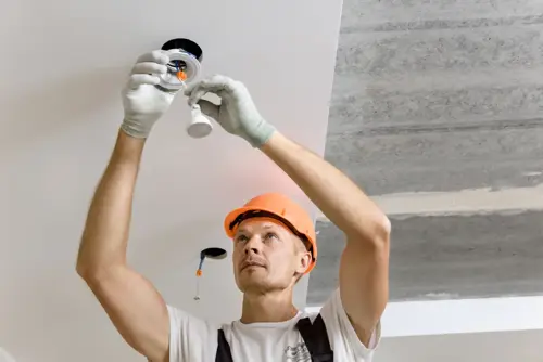 An ARS technician reaching to the ceiling, installing recessed lighting for a commercial company.