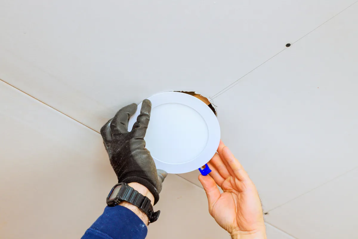 An ARS technician's hands are installing a recessed lighting fixture in a home. 