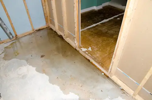 View of a concrete basement floor full of water caused by sewer backflow due to a clogged sanitary drain.