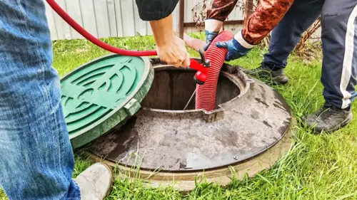Service technicians cleaning a septic tank using a vacuum hose in a backyard.