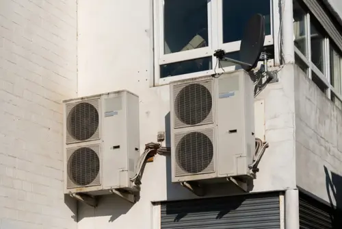 Exterior wall-mounted split-level air conditioning condenser units installed outside a multi-level residential building.