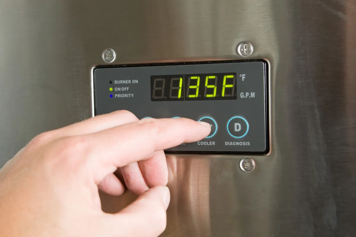 Close-up of a person adjusting the temperature on a digital control panel of a water heater, with a temperature of 135°F displayed on the screen.